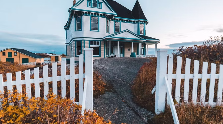 A big house on the hill with white wooden fence on the entrance.